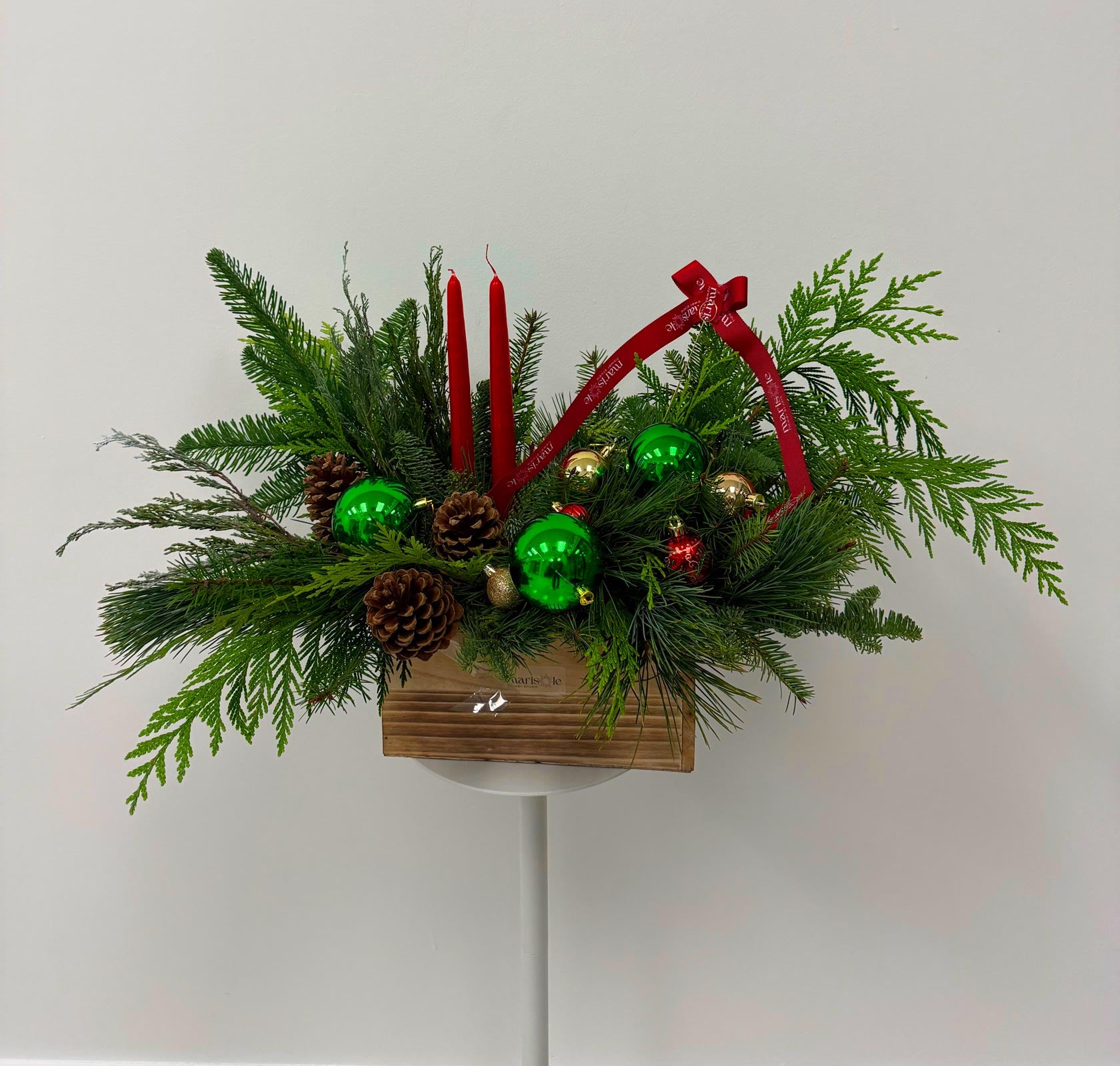 Decorative Christmas arrangement with greenery, ornaments, and a red basket on a white background