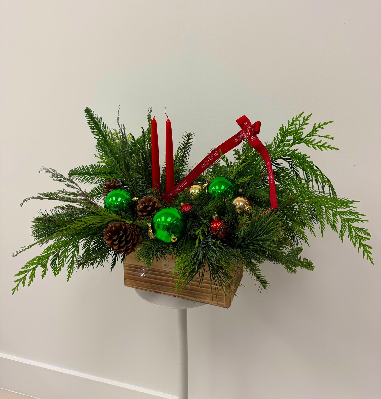 Decorative Christmas arrangement with greenery, candles, and ornaments on a white wall.
