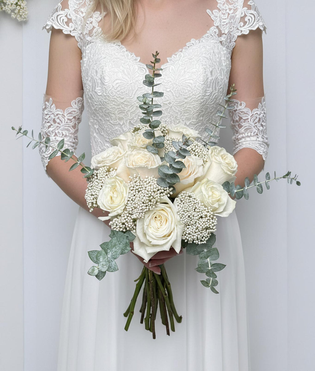 Bride holding a bouquet of white flowers with greenery against a plain background