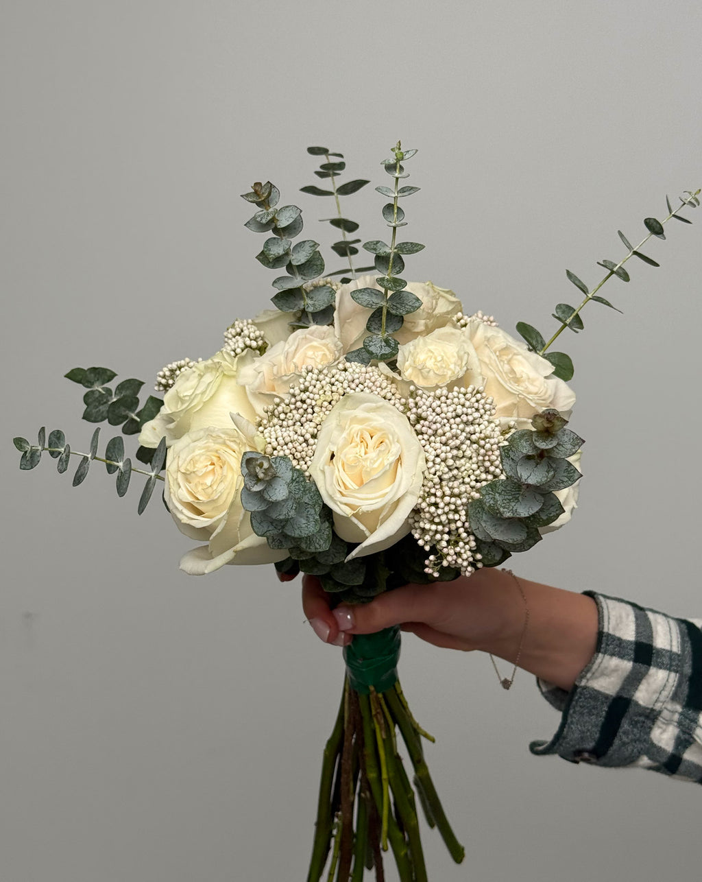 Bouquet of white roses and eucalyptus held by a person against a gray background