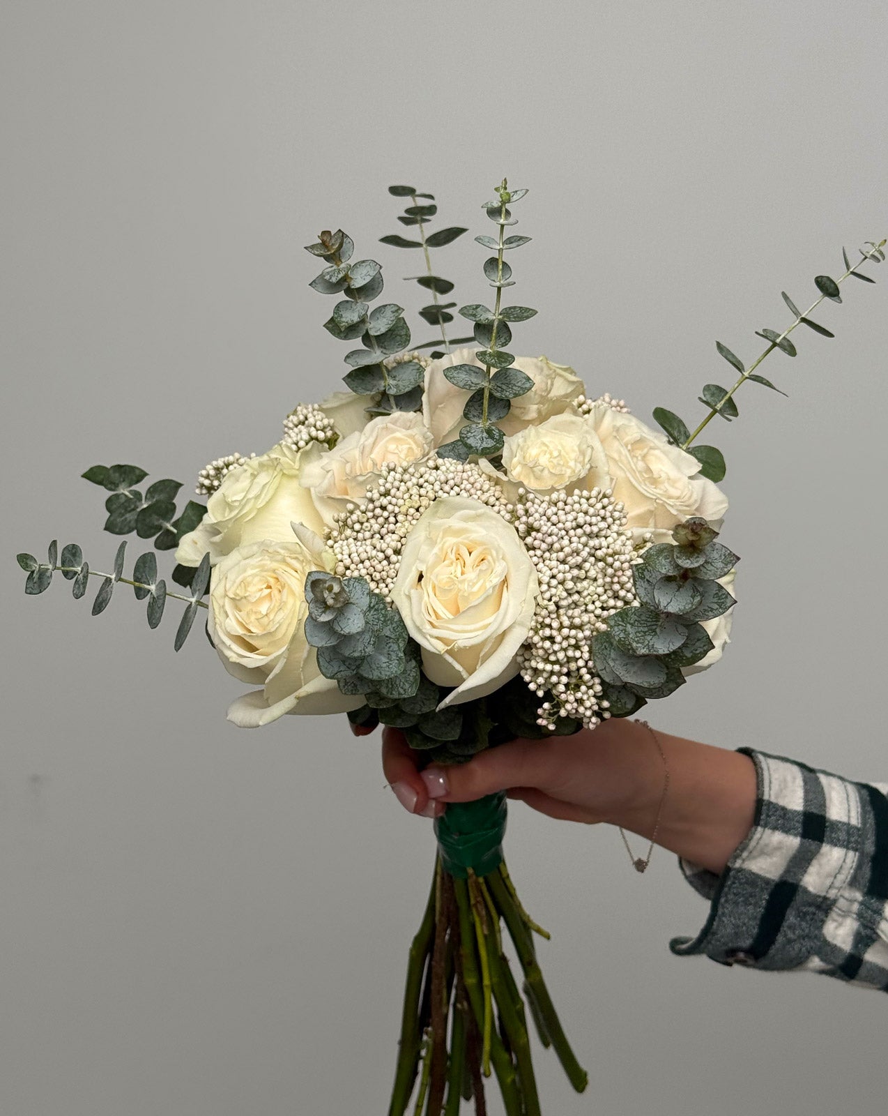 Bouquet of white roses and eucalyptus held by a person against a gray background