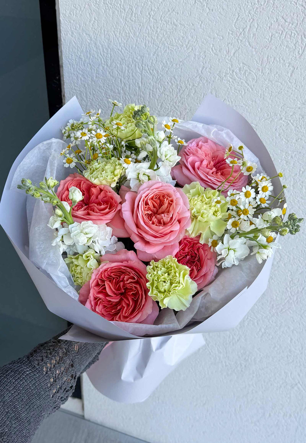 Cottage Blooms bouquet with pink garden roses, green carnations, white stock, and chamomile wrapped in white paper