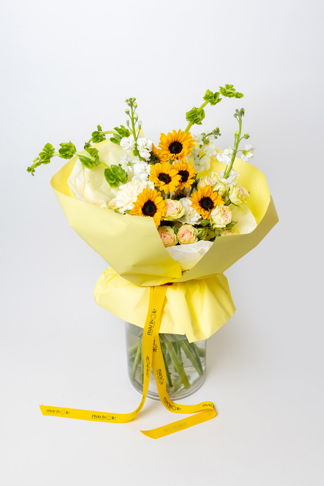Bouquet of flowers with sunflowers and white flowers wrapped in yellow paper on a light gray background