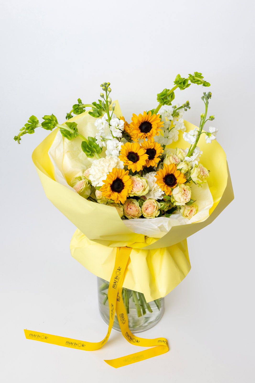 Bouquet of sunflowers and white flowers wrapped in yellow paper with a yellow ribbon on a light gray background