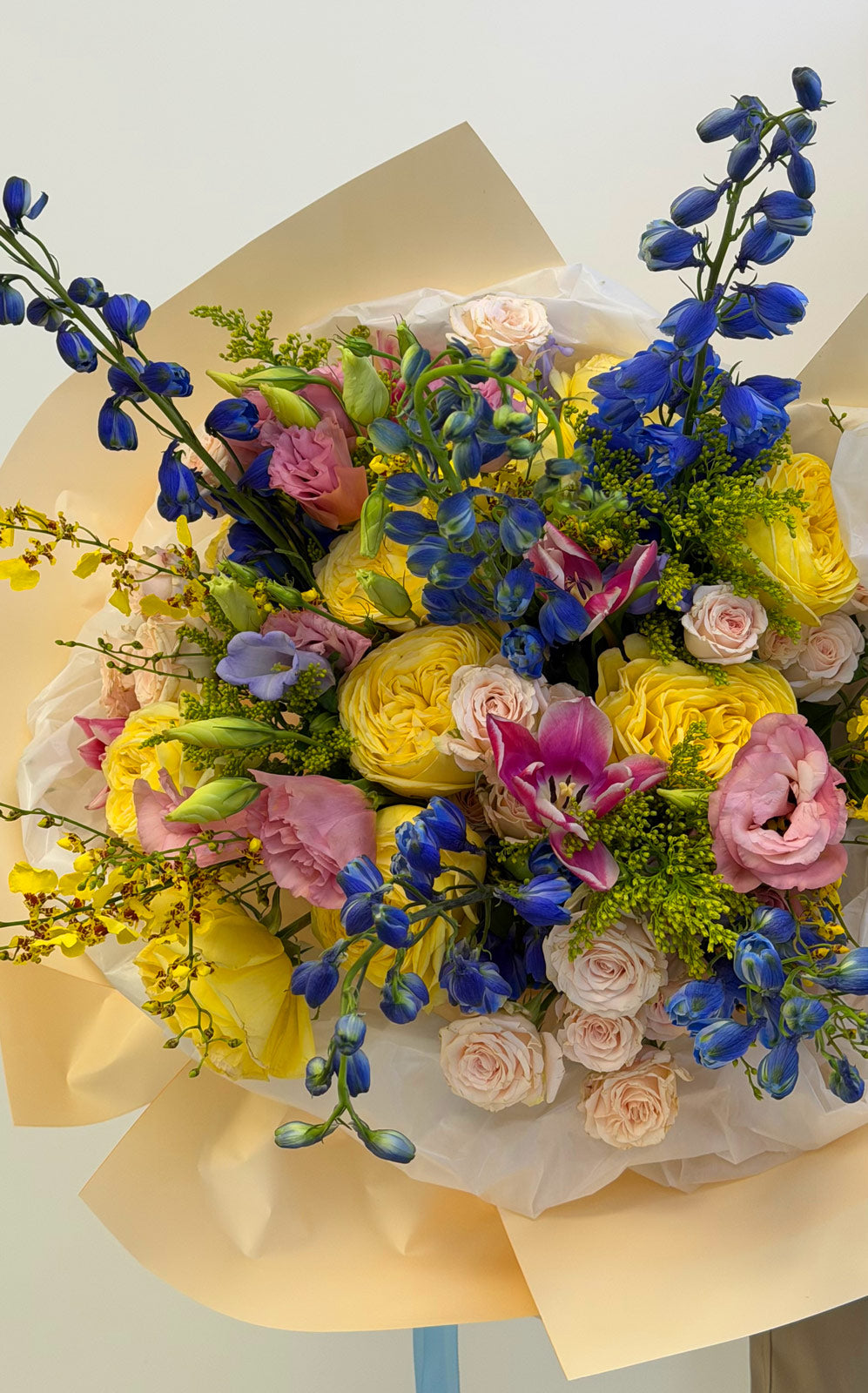 Colorful bouquet of flowers with yellow, pink, blue, and green colors on a light background.