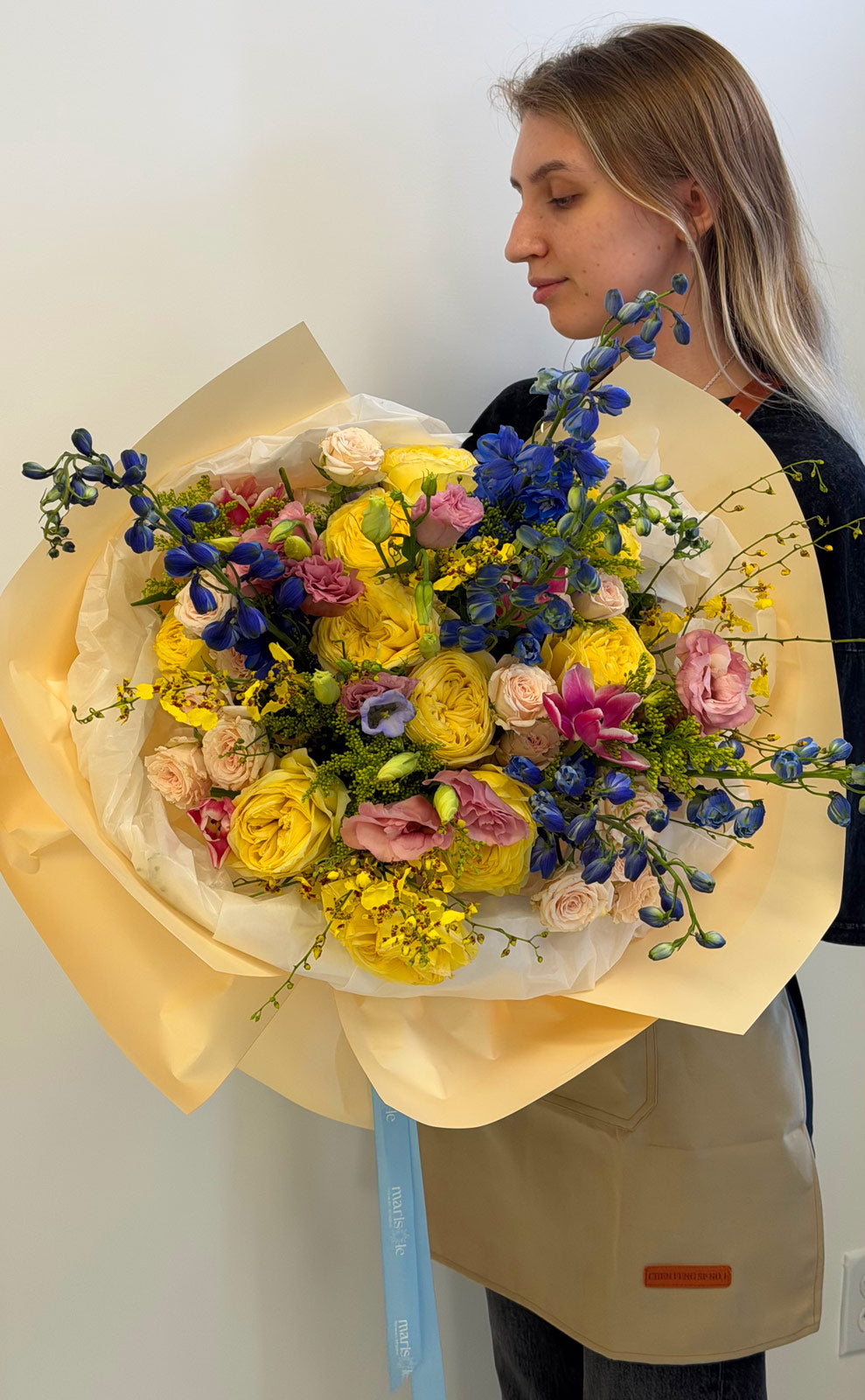 Person holding a large bouquet of flowers wrapped in yellow paper against a plain background