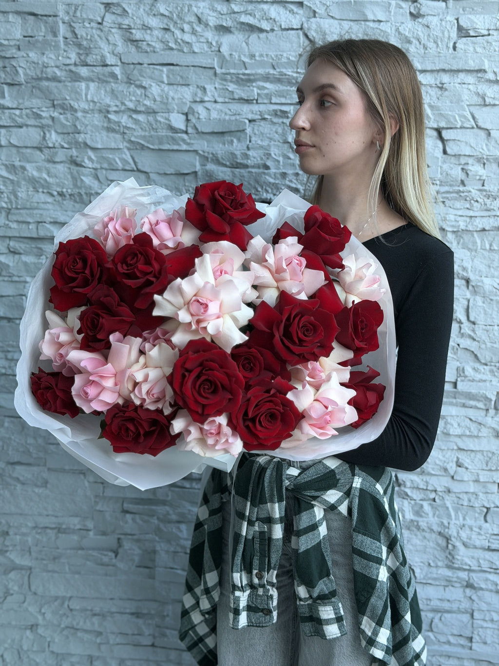 Woman holding a large bouquet of red and pink french roses against a stone wall.