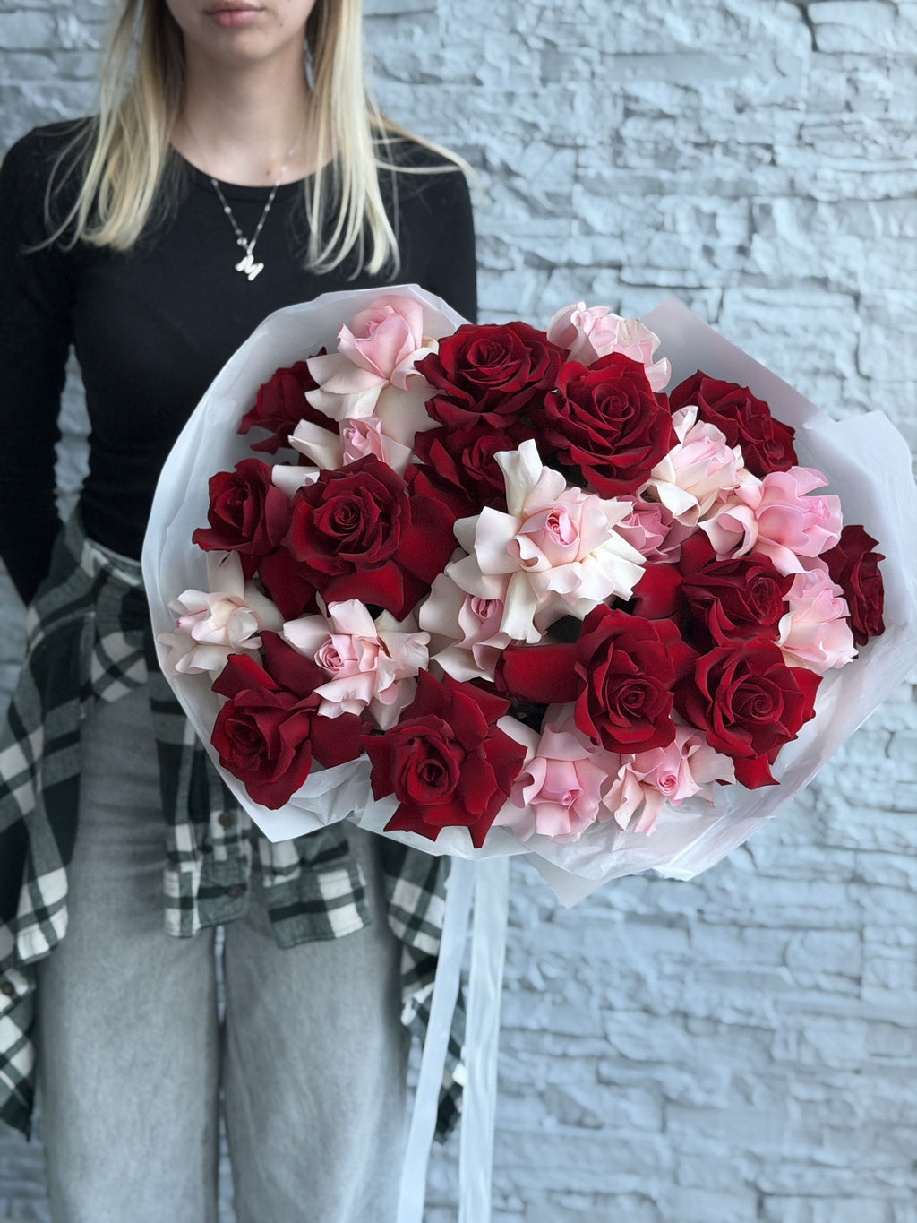 Bouquet of red and pink french roses held by a person against a light brick wall.