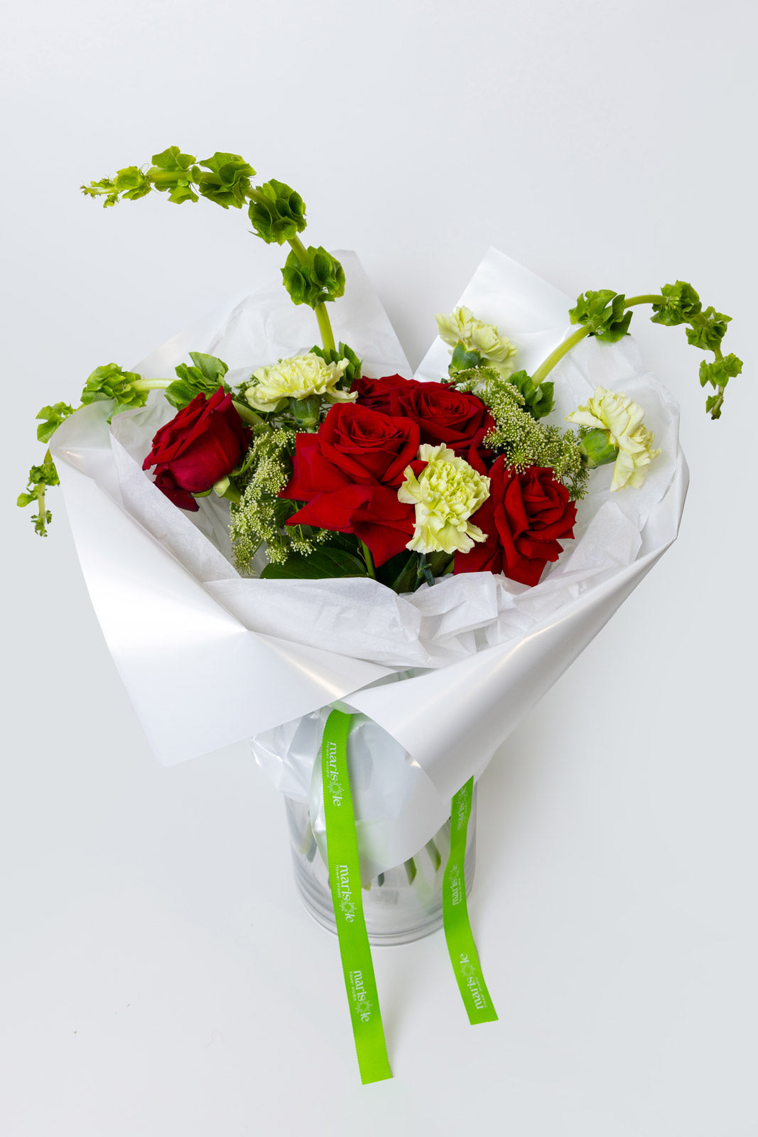 Bouquet of red and green flowers wrapped in white paper with a green ribbon on a white background