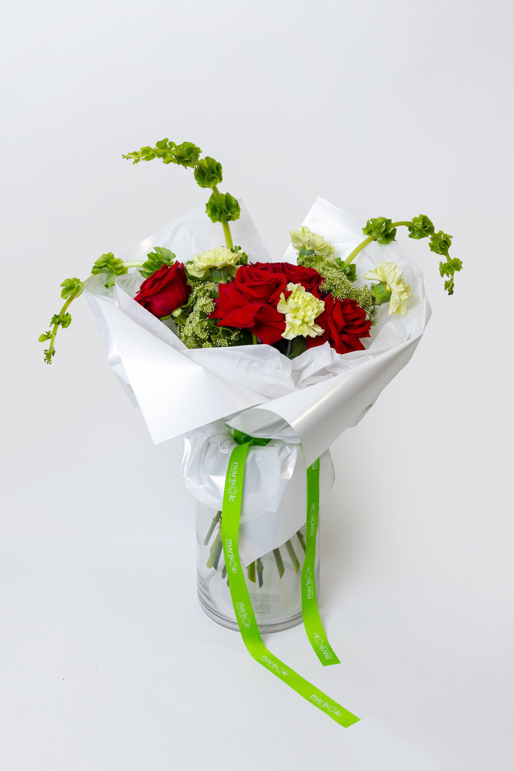 Bouquet of red and white flowers wrapped in white paper with a green ribbon on a light gray background