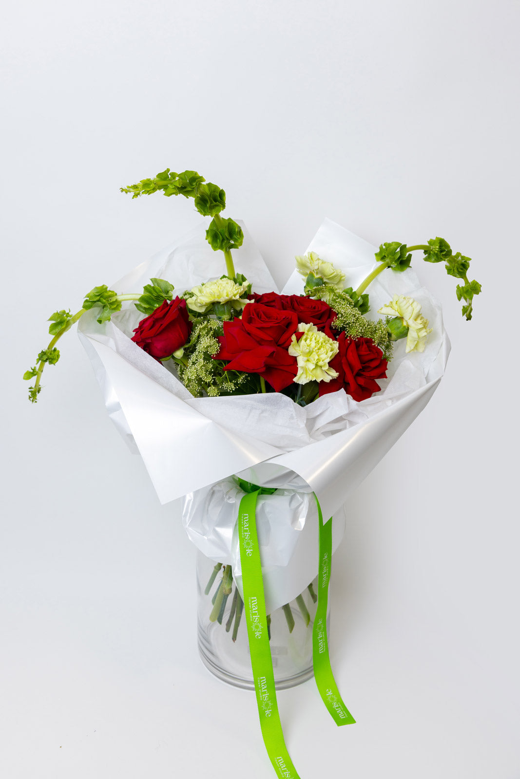 Bouquet of red and white flowers wrapped in white paper with a green ribbon on a light gray background