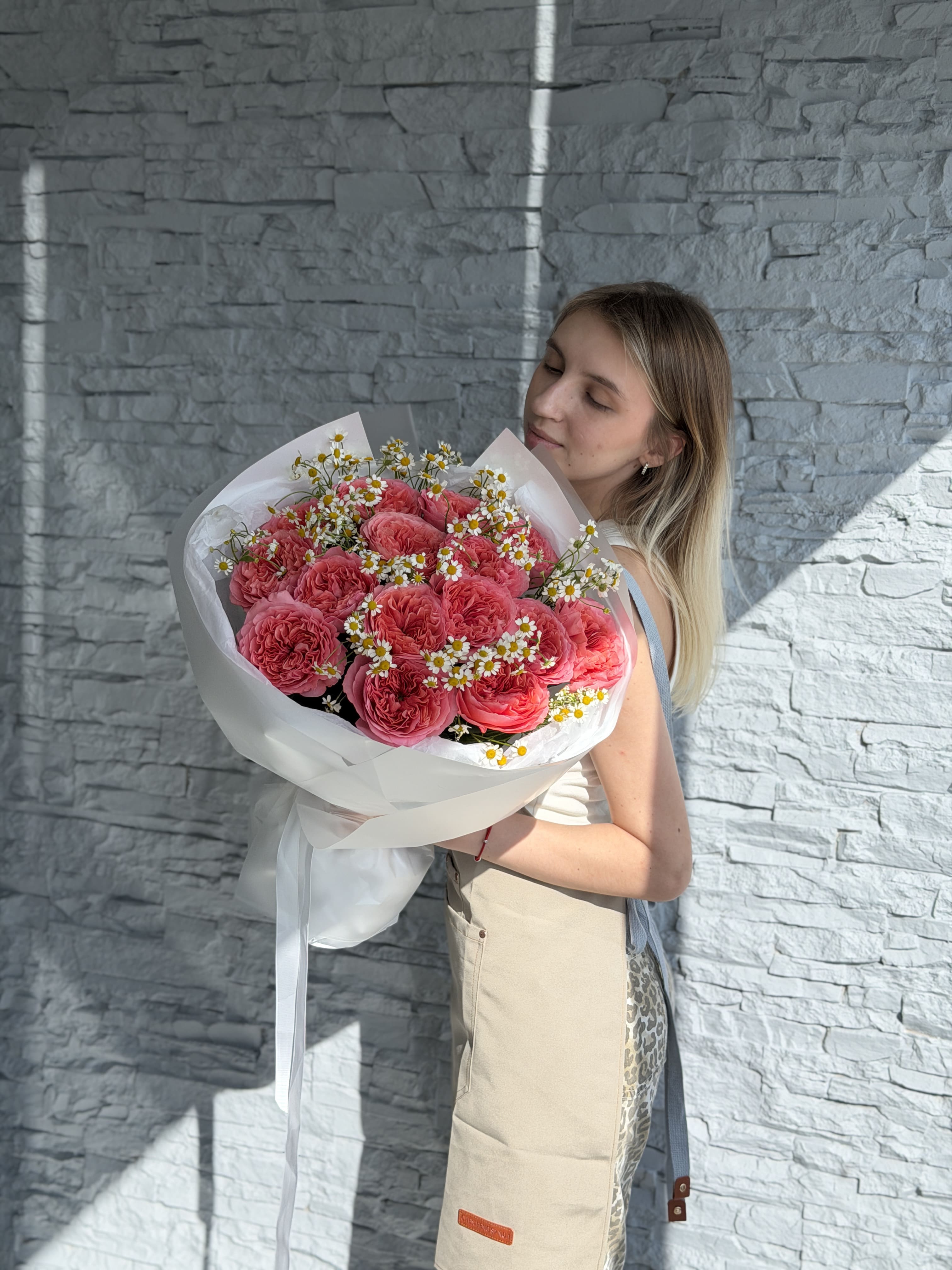 Woman holding a bouquet of red flowers against a stone wall.