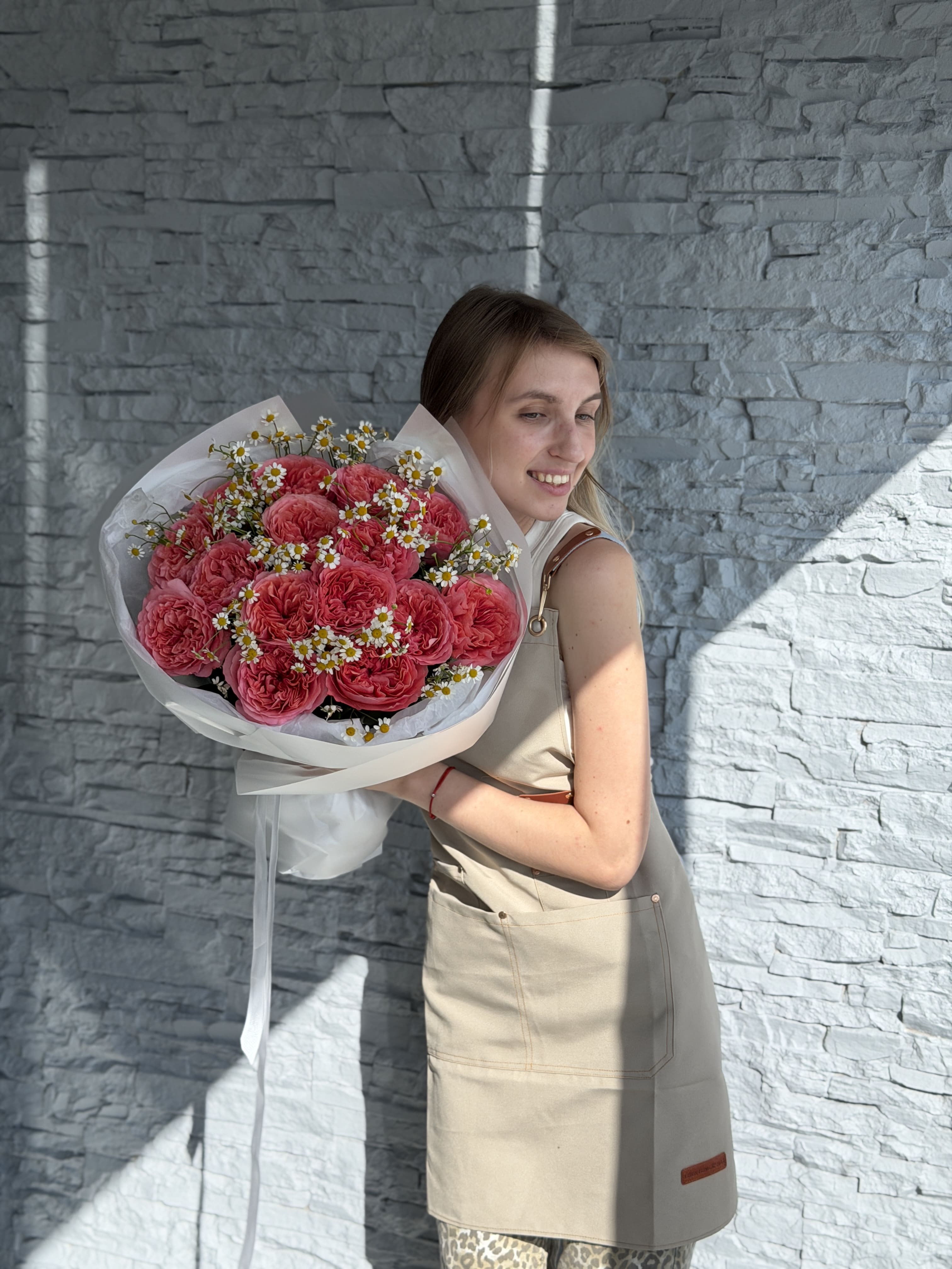 Woman holding a large bouquet of red flowers against a stone wall.