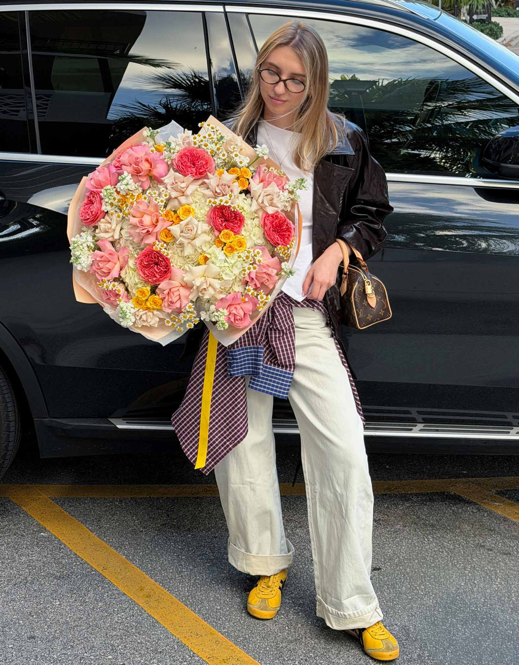 Full-length view of a woman holding a large Golden Hour Bouquet featuring French roses, garden roses, hydrangeas, stock, and chamomile.