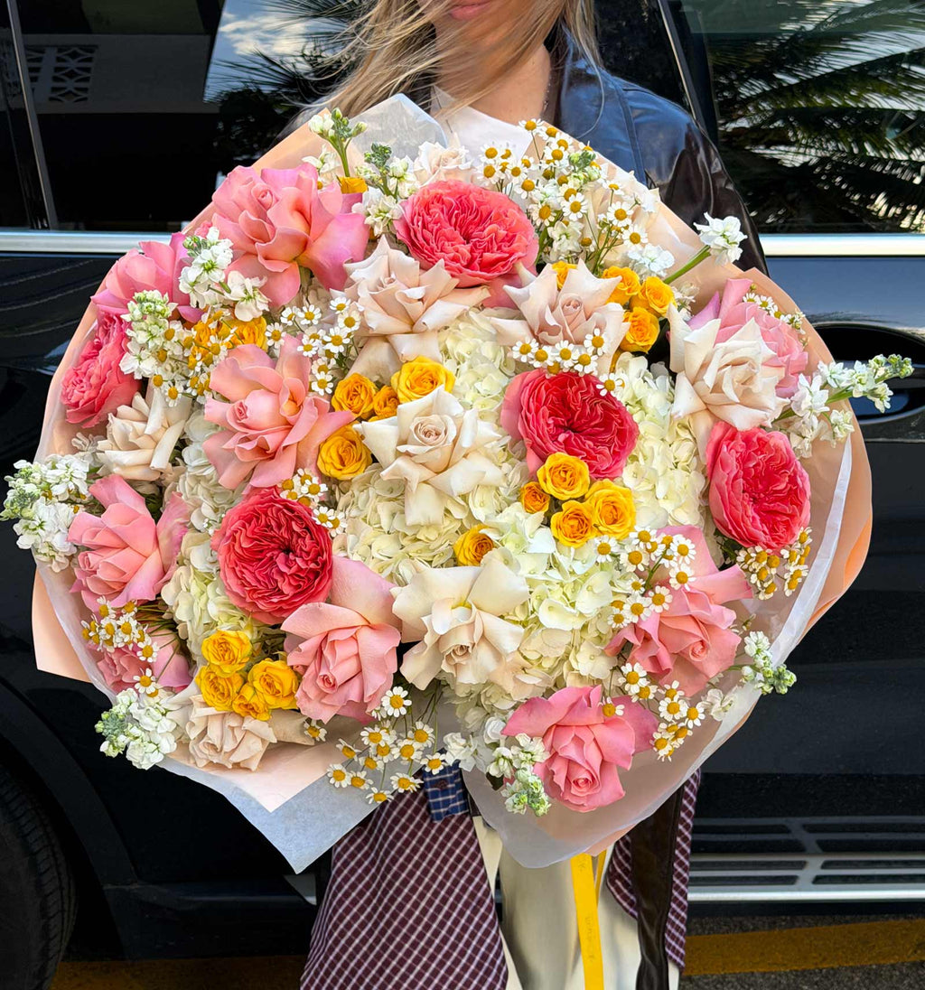 Woman holding a large Golden Hour Bouquet with pink garden roses, ivory hydrangeas, yellow spray roses, French roses, stock, and chamomile.