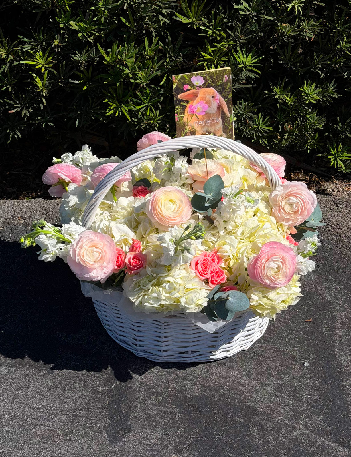 White basket filled with pink and white flowers on a dark surface with greenery in the background