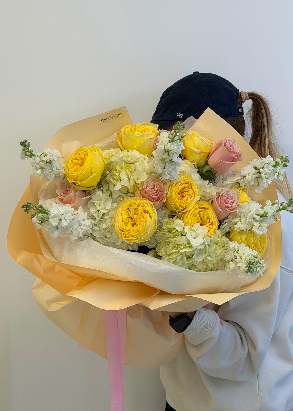 Bouquet of yellow and pink roses with white flowers wrapped in yellow paper, held by a person.