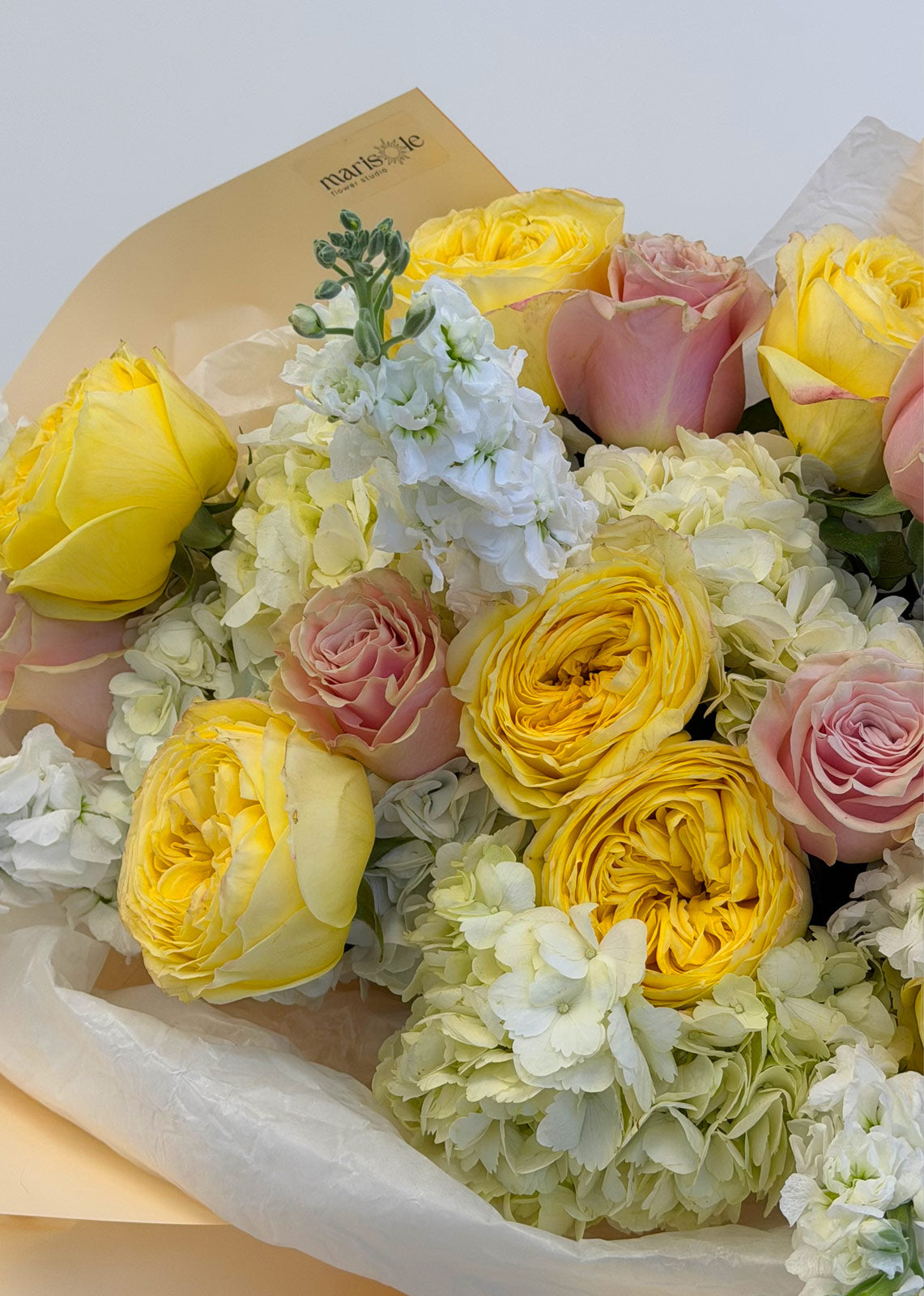 Bouquet of yellow and pink roses with white flowers in a paper wrap.