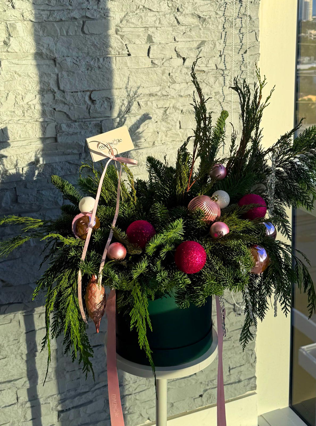 Decorative floral arrangement with ornaments on a stand against a stone wall.
