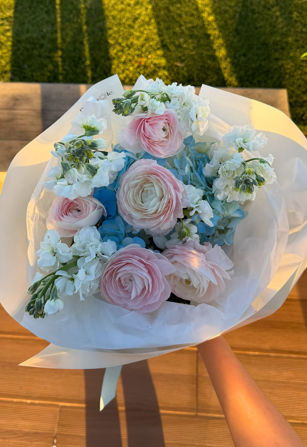 Bouquet of flowers with pink and blue tones held by a person outdoors.