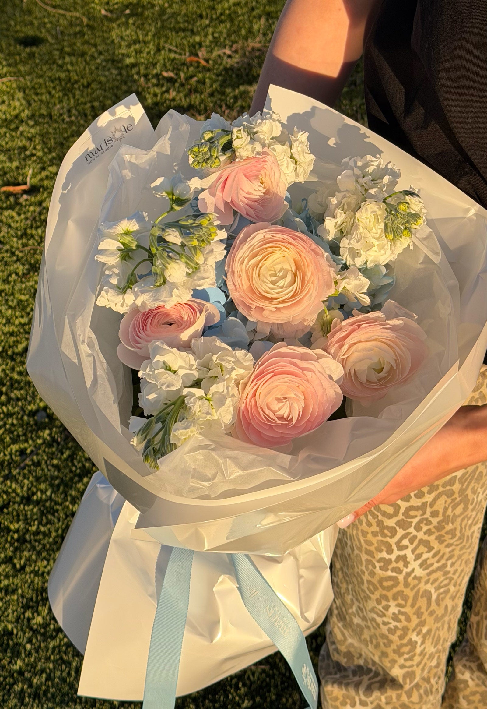 Bouquet of pink and white flowers held by a person on grass