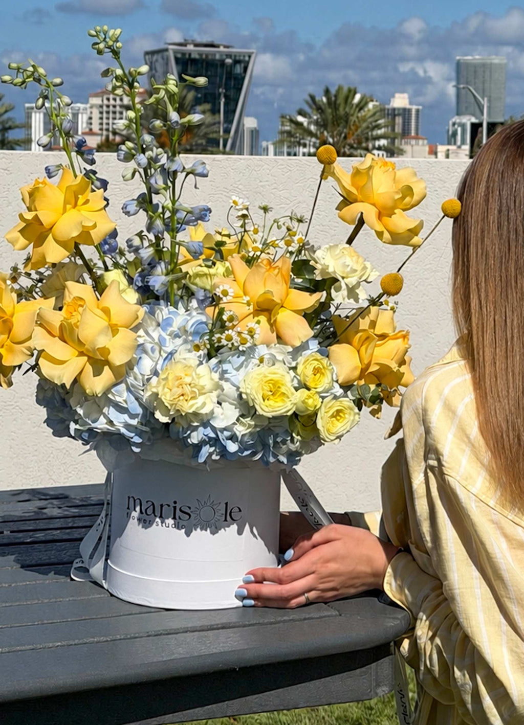 Person holding a bouquet of yellow and white flowers with a cityscape in the background