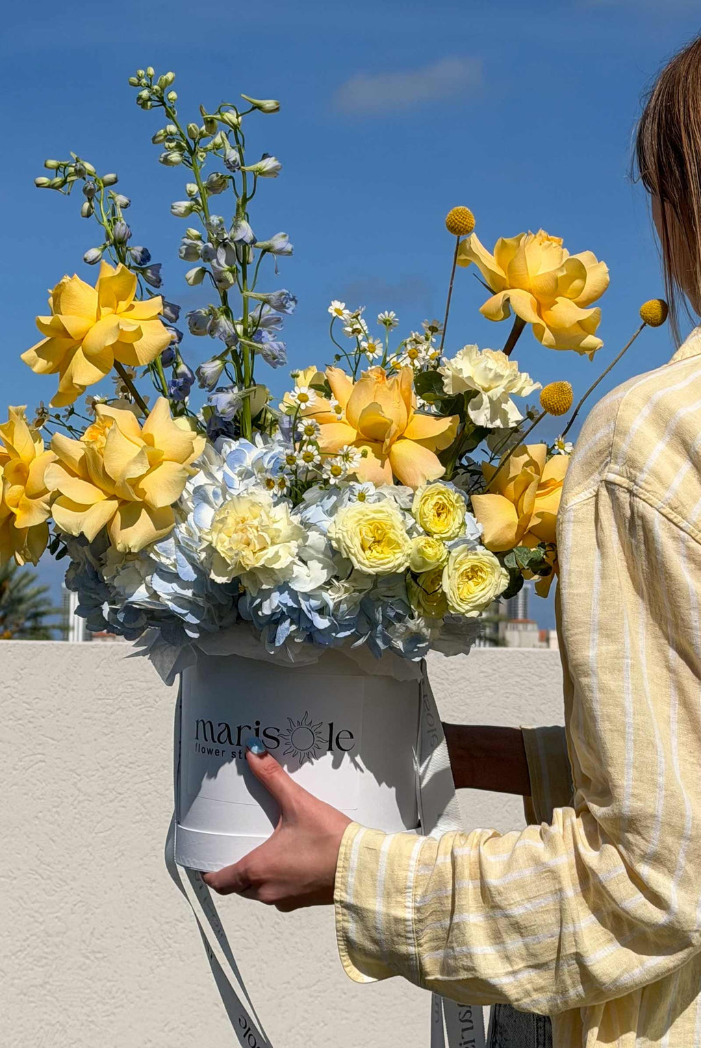 Side view of the Limoncello Box by Marisole Flowers with yellow French roses, hydrangea, delphinium, and craspedia.