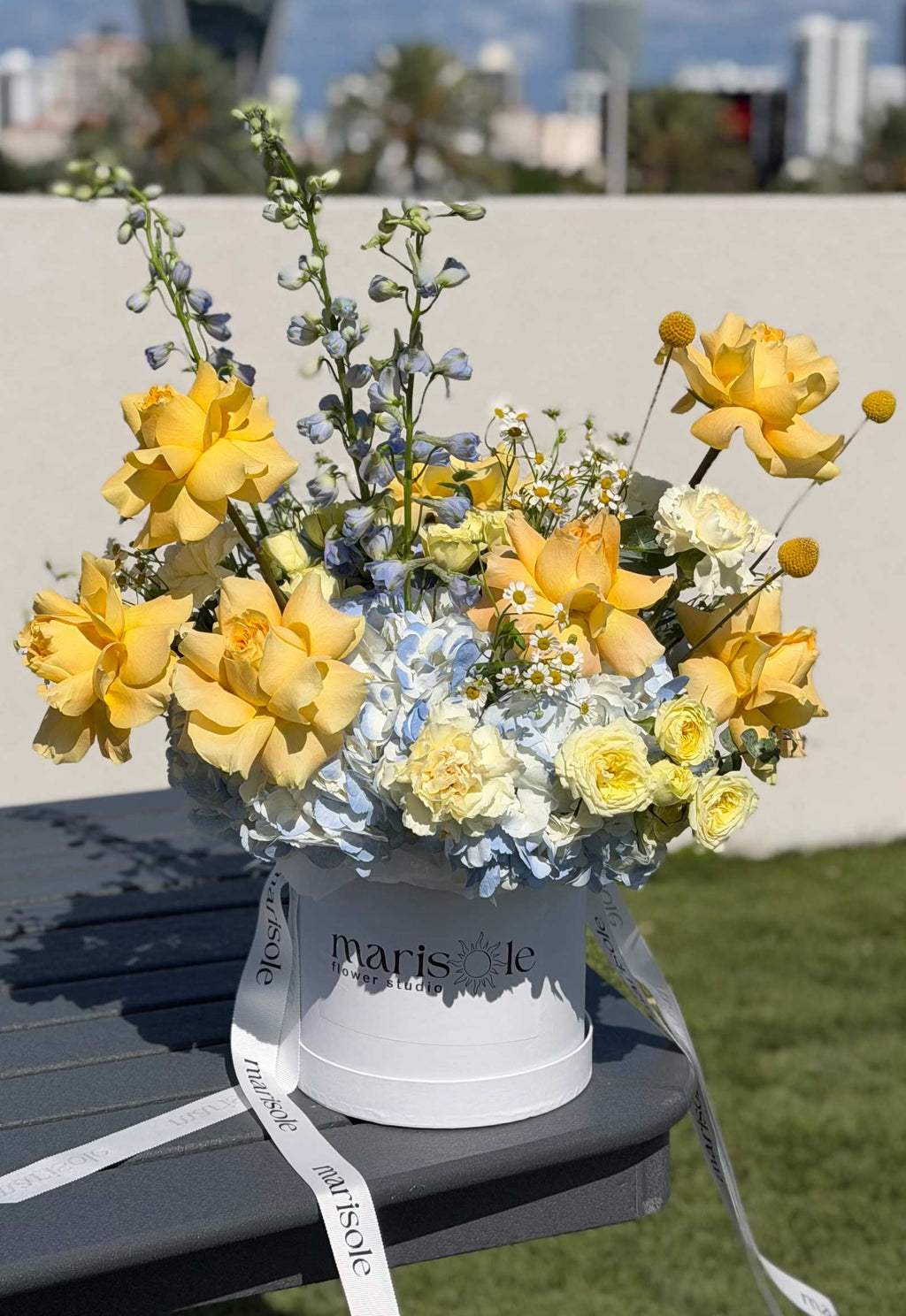 Limoncello Box flower arrangement with French roses, hydrangea, delphinium, chamomile, spray roses, carnations, and craspedia.