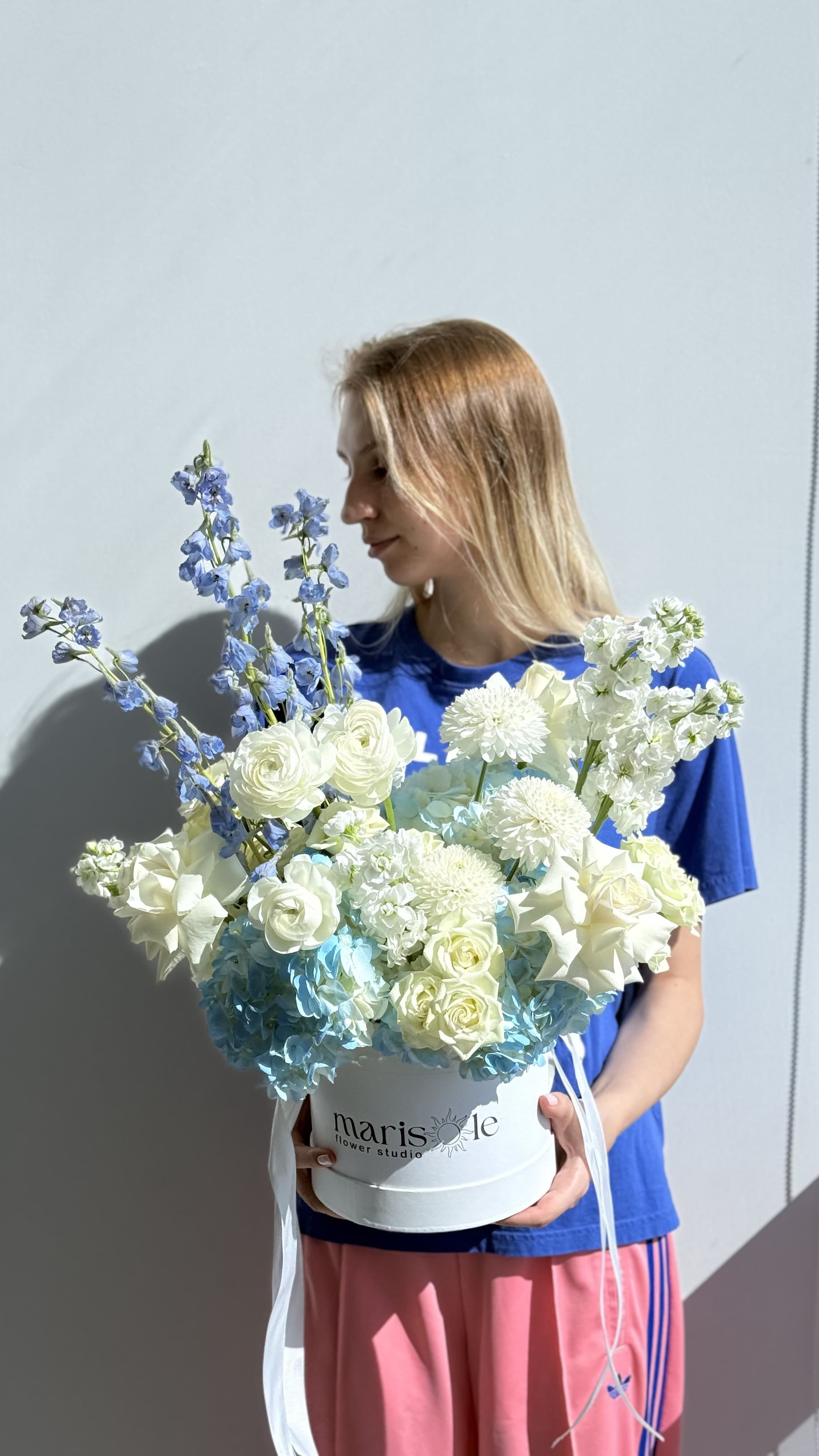 Woman holding a bouquet of flowers with a 'marisole flowers' box against a light gray background