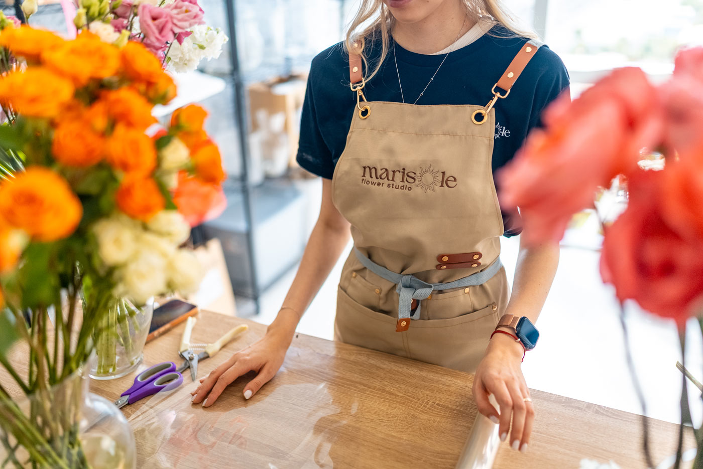 Florist at work in Marisole Flower Studio, preparing floral arrangements at a worktable surrounded by fresh flowers.