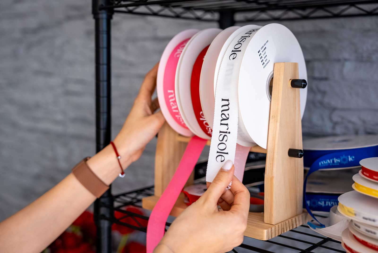 Person selecting ribbons from a holder with 'Marisole Flowers' branding.