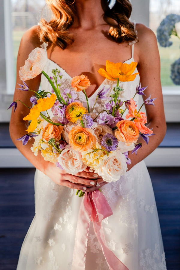 Bride holding a colorful bouquet with flowers and ribbons.