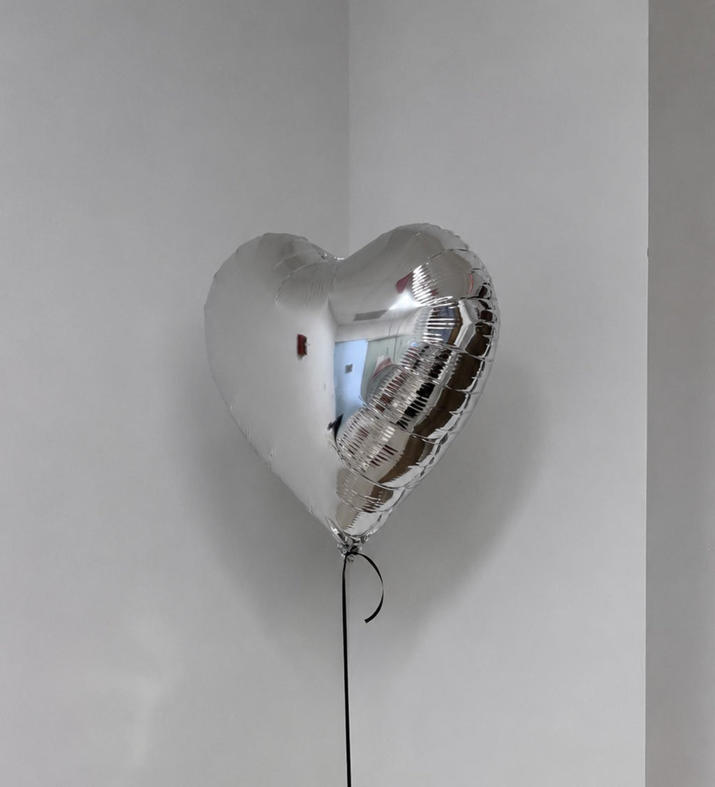 Silver heart-shaped balloon against a plain white wall