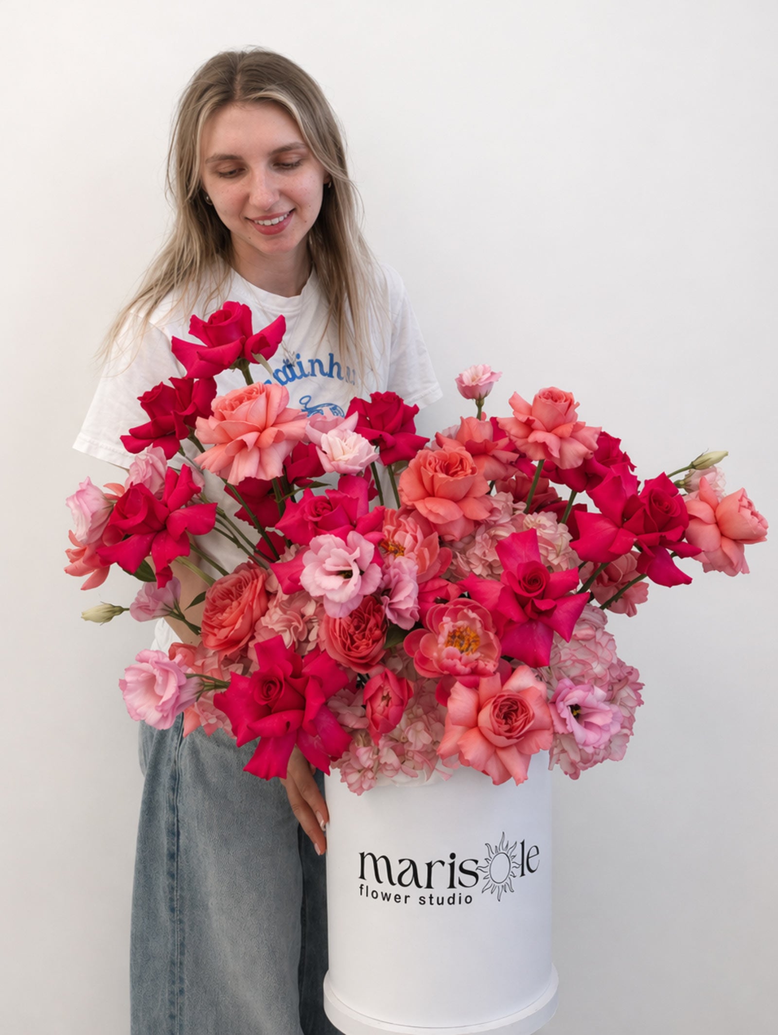 Person holding a large bouquet of pink and red flowers in a container with 'Marisole Flower Studio' branding.