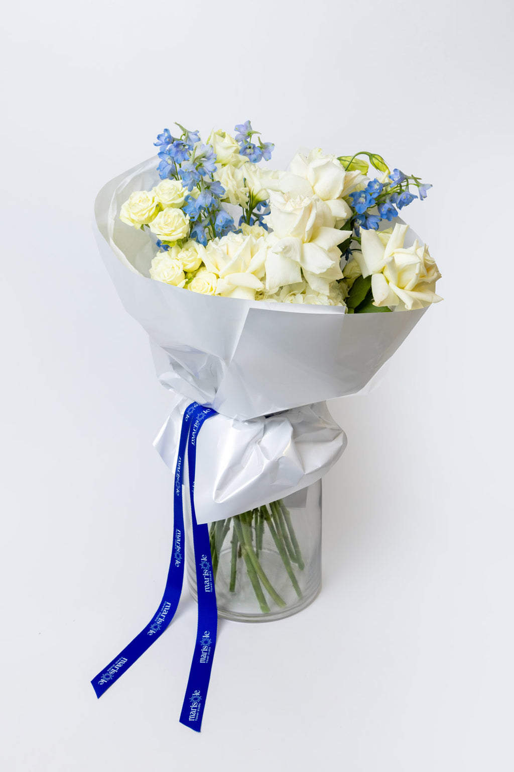 Bouquet of white flowers with blue accents wrapped in white paper and a blue ribbon on a white background