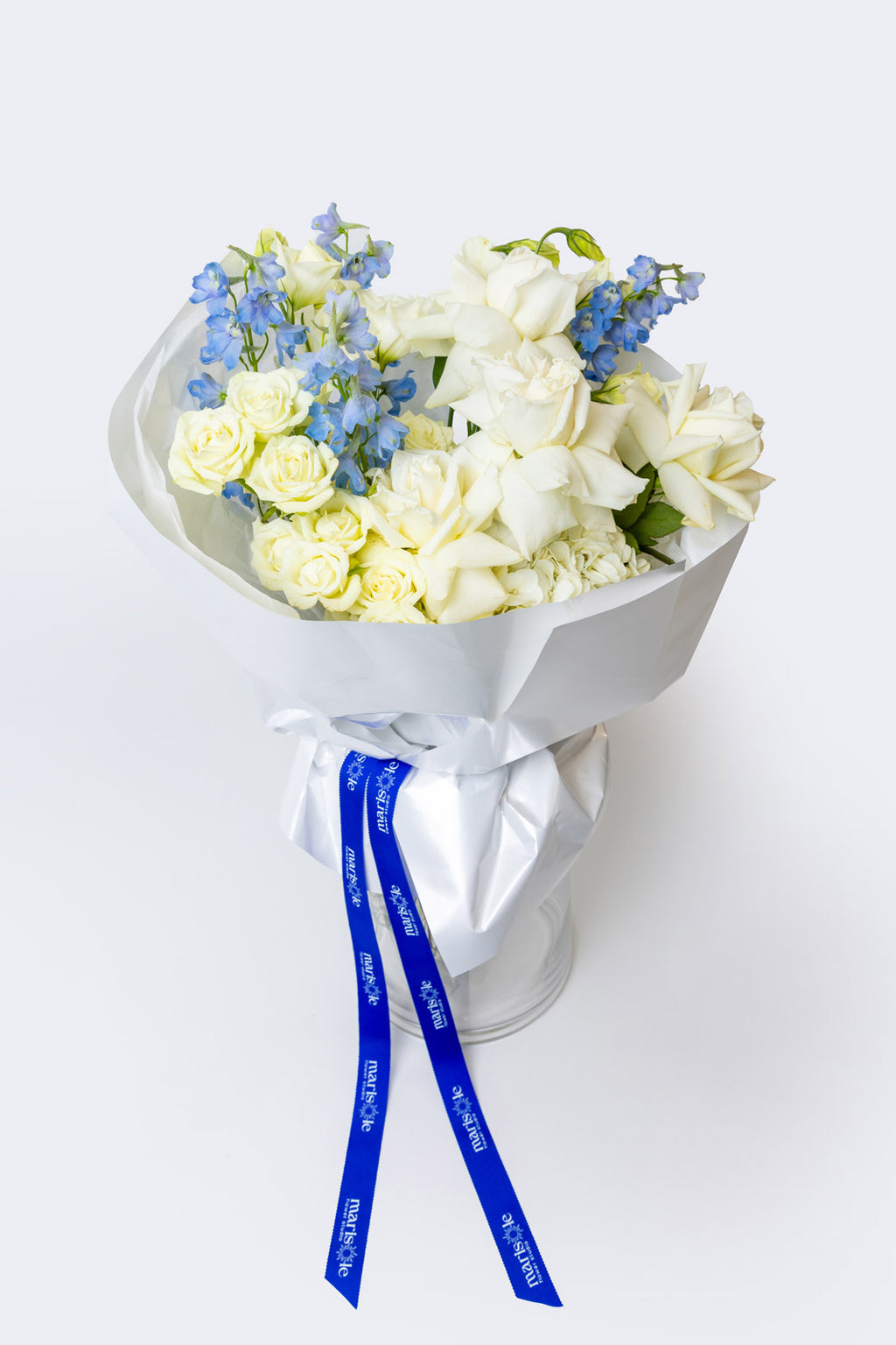 Bouquet of white and yellow flowers with blue accents in a clear container on a white background