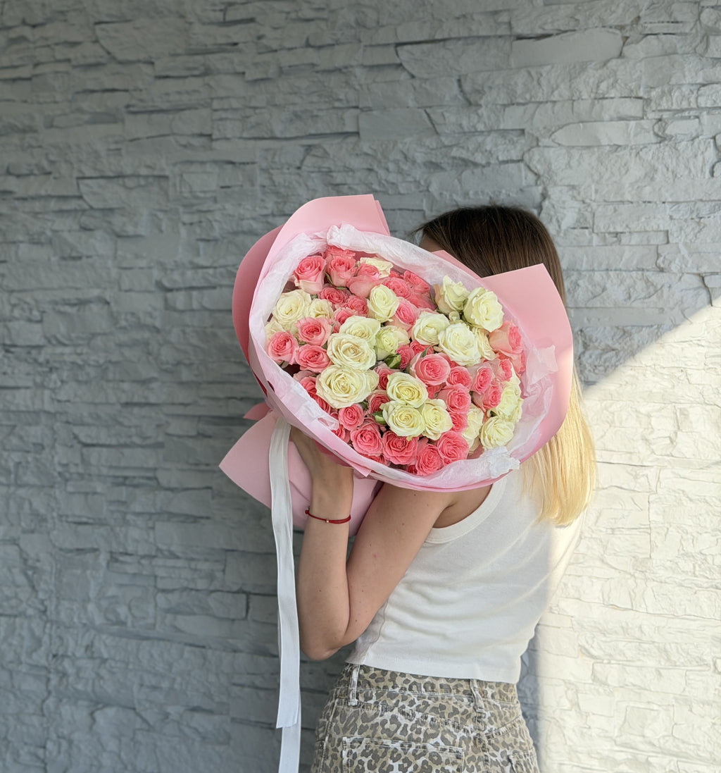 Person holding a bouquet of pink and white roses against a gray stone wall.