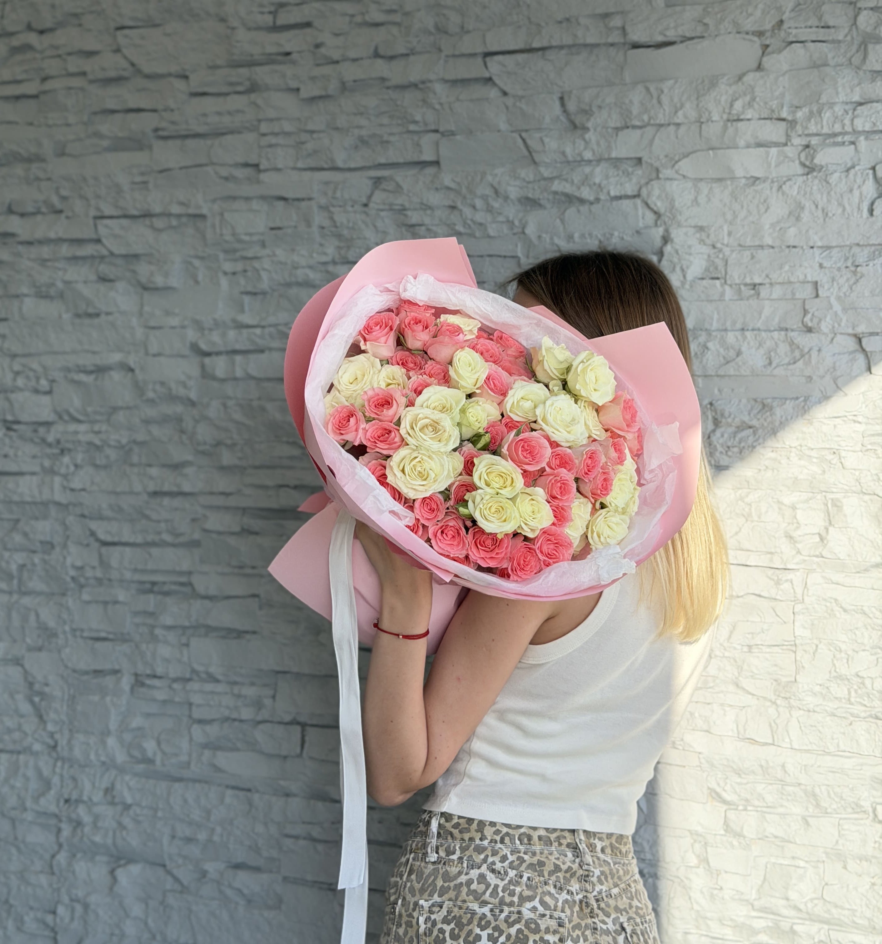 Person holding a bouquet of pink and white roses against a gray stone wall.