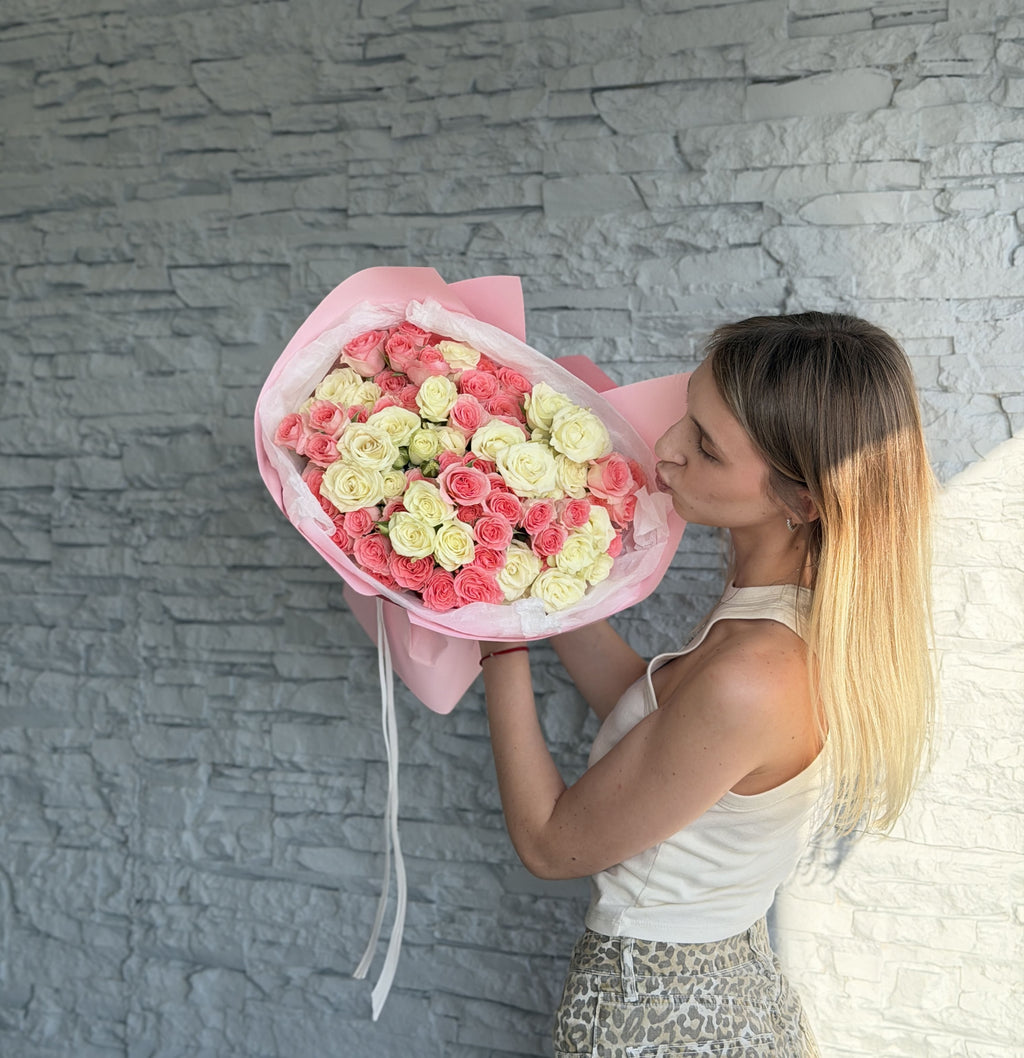 Woman holding a bouquet of pink and white flowers against a gray stone wall.