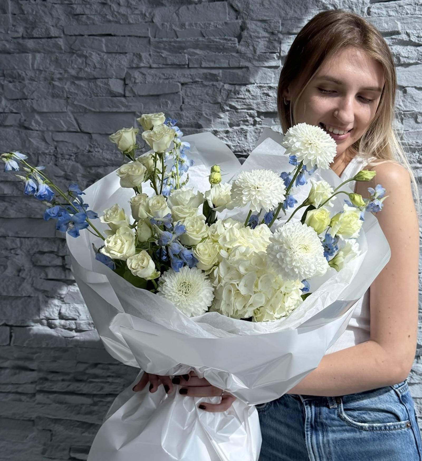 Woman holding a bouquet of white and blue flowers against a stone wall.