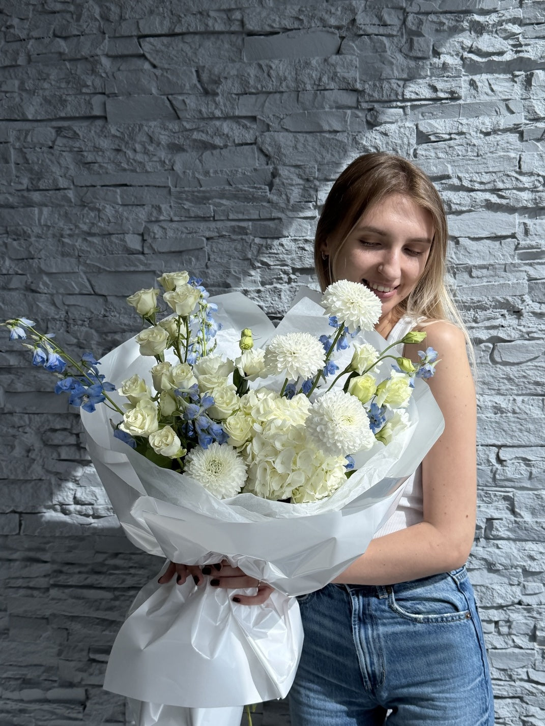 Woman holding a bouquet of flowers against a stone wall.