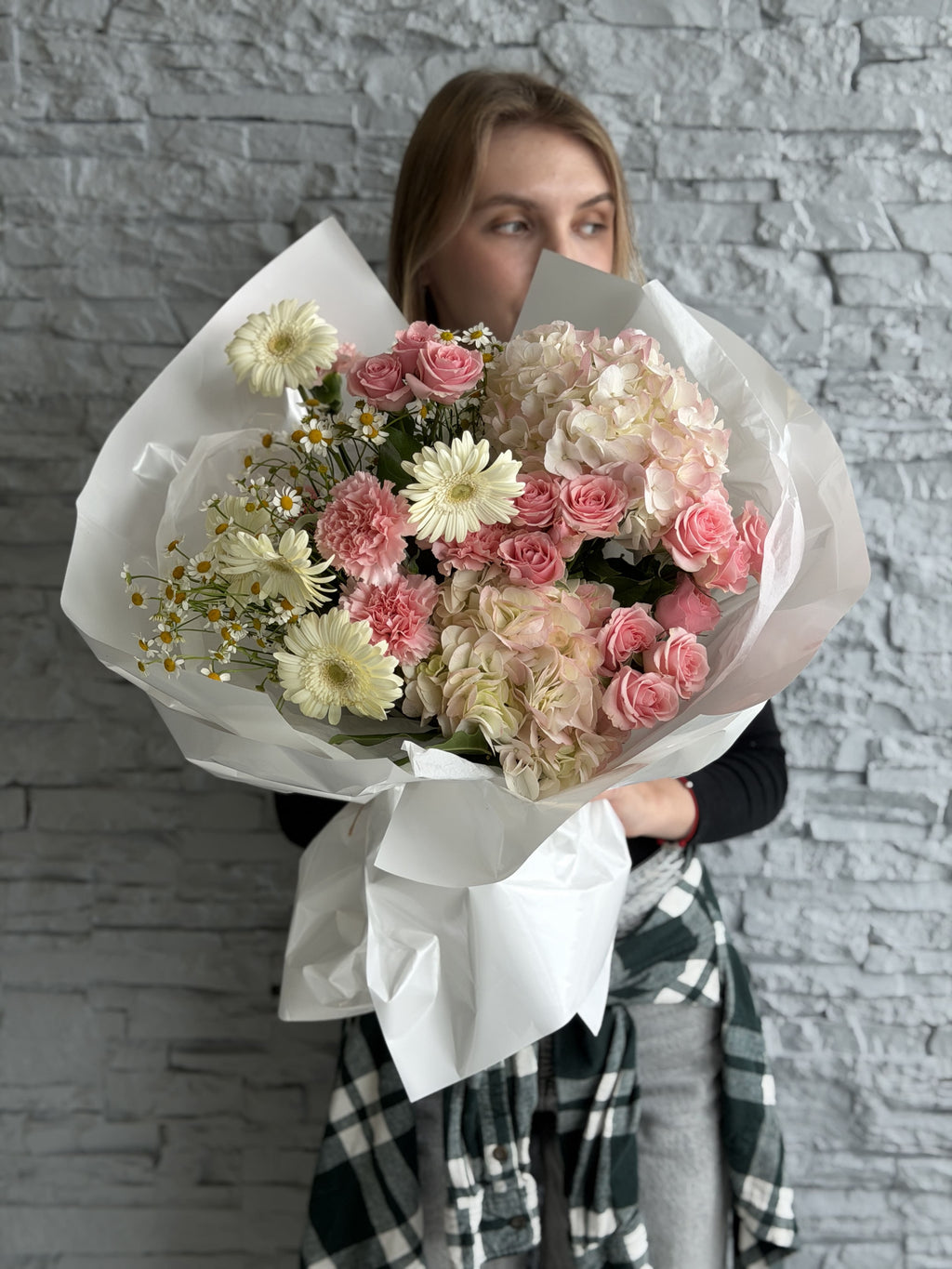 Person holding a large bouquet of flowers against a gray stone wall.