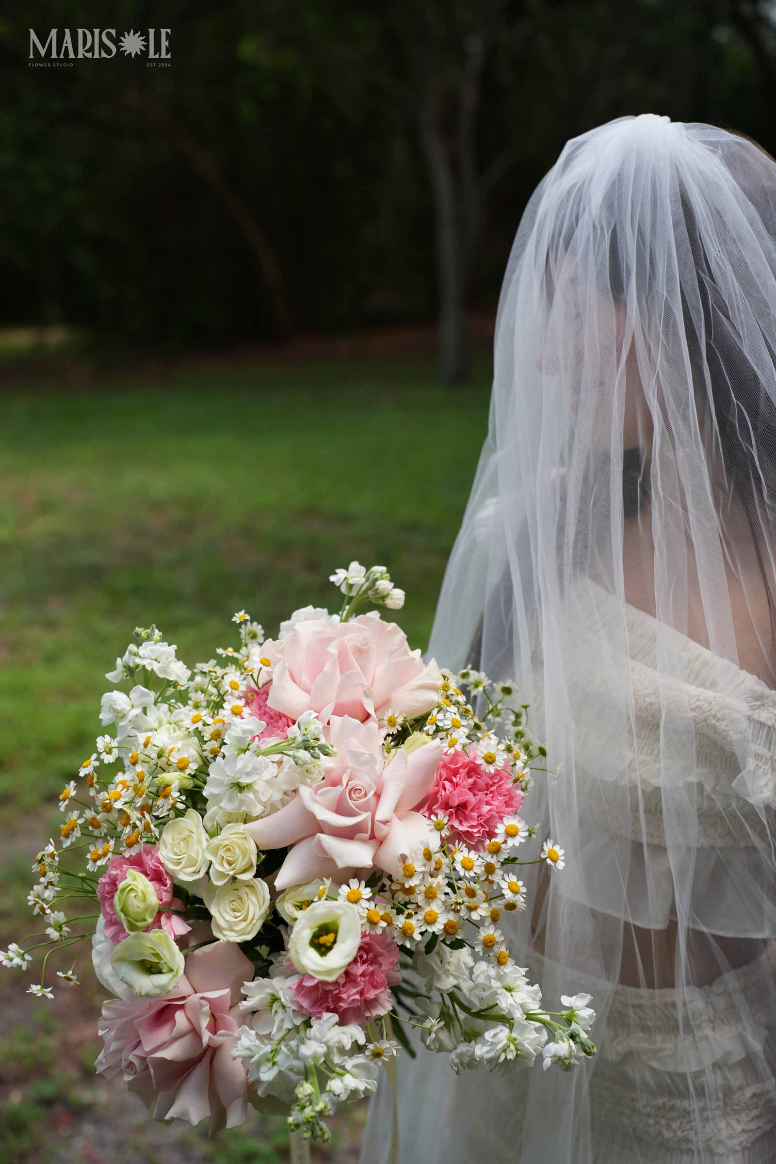 Bride in a veil holding a pastel wedding bouquet in a garden