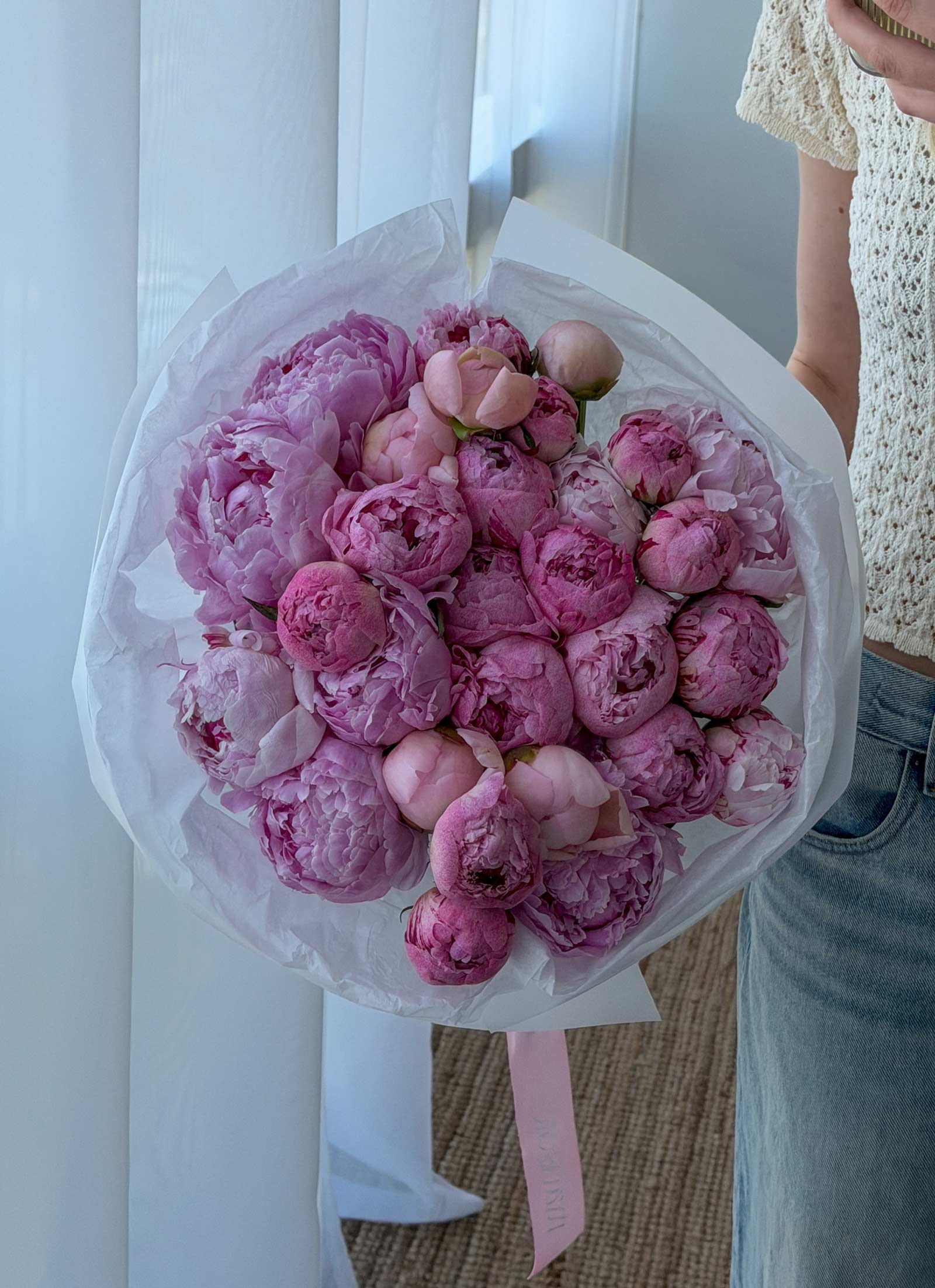 Bouquet of pink peonies wrapped in white paper held by a person.