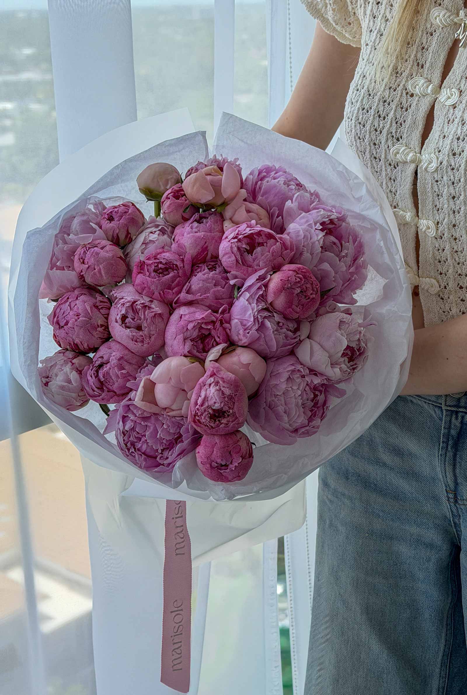 Bouquet of pink peonies held by a person with a blurred background