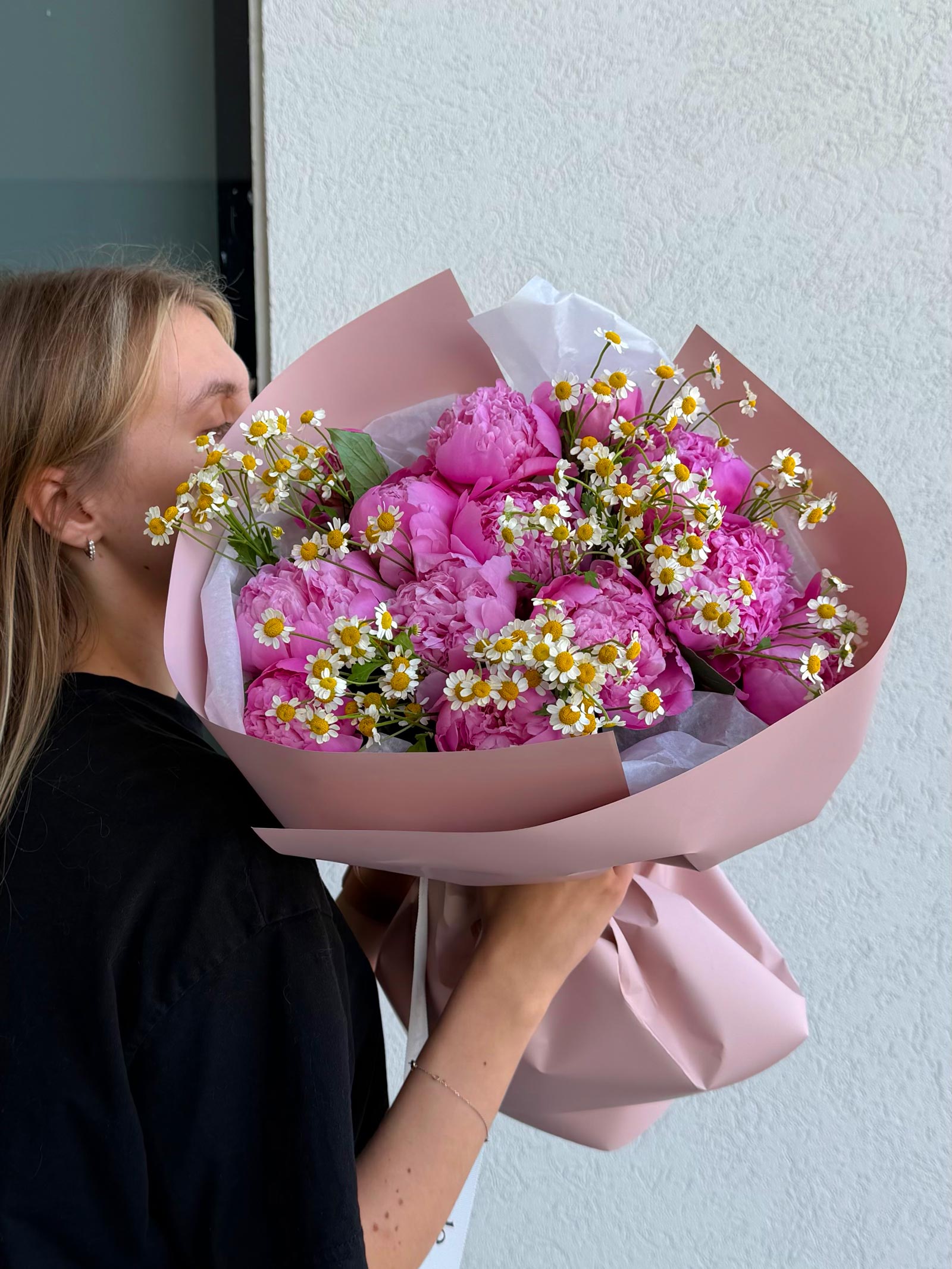 Person holding a bouquet of pink flowers with white accents against a light background