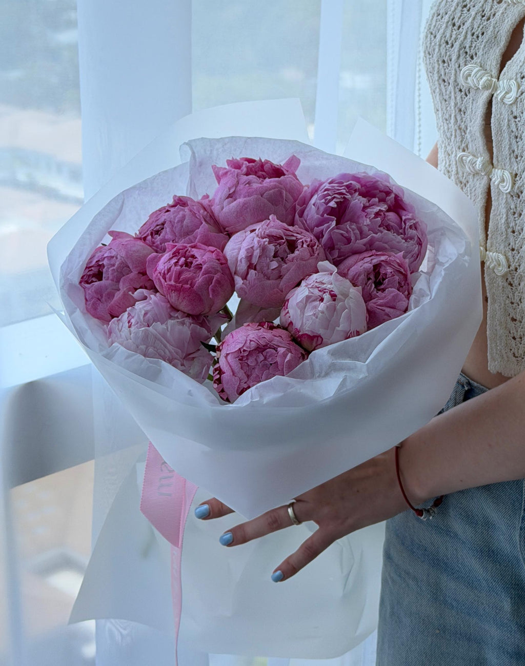 Close-up of a pink peonies bouquet wrapped in white paper with a pink Marisole ribbon.