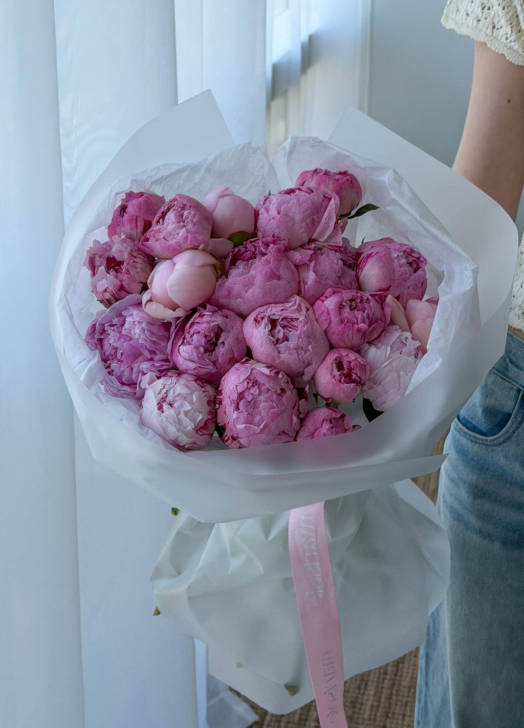 Bouquet of pink peonies held by a person with a white background