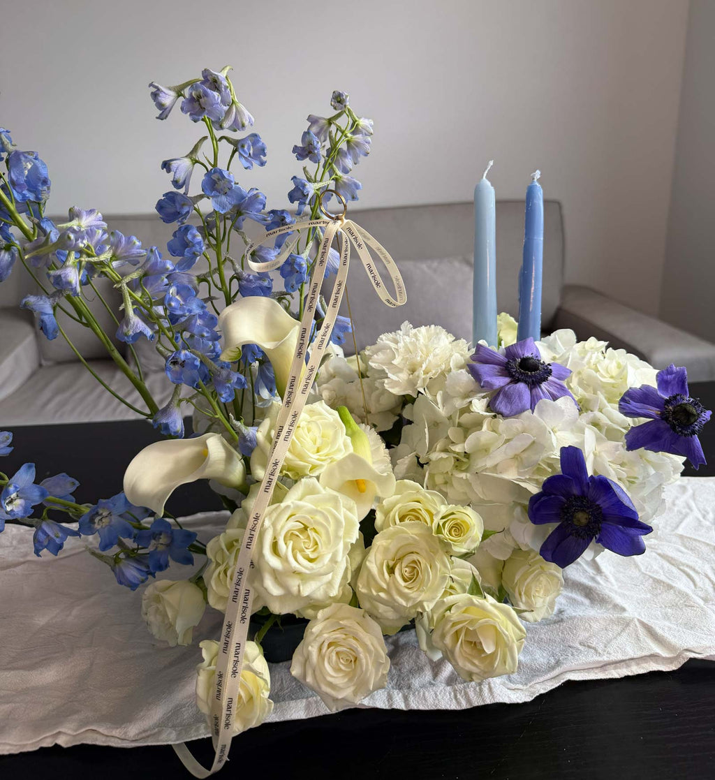 Bouquet of white and blue flowers with candles on a table.