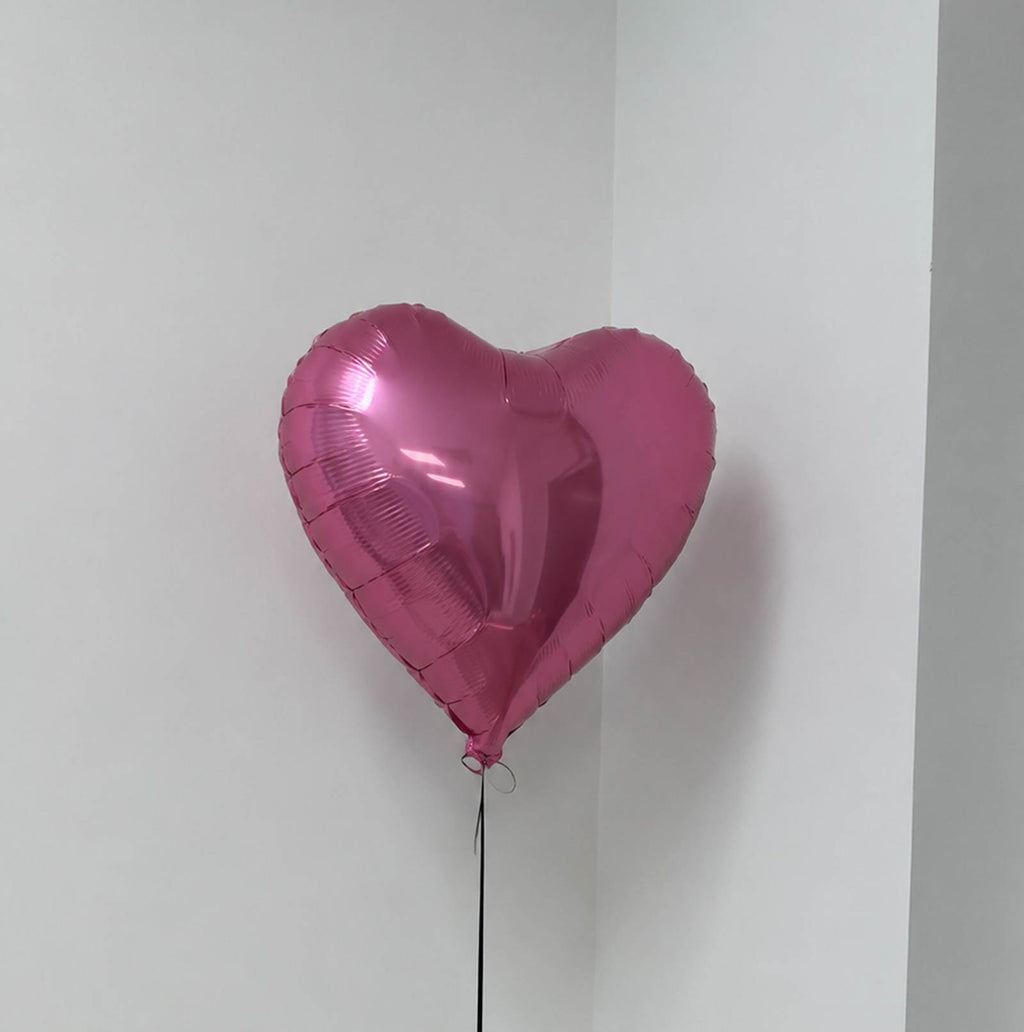 Pink heart-shaped balloon against a white wall
